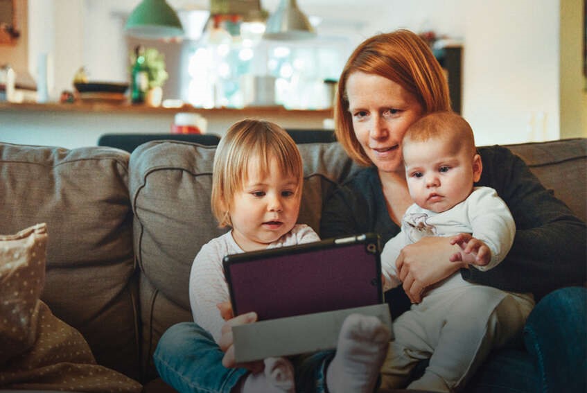 Vrouw zit met twee kleine kinderen op de bank te kijken naar ipad.